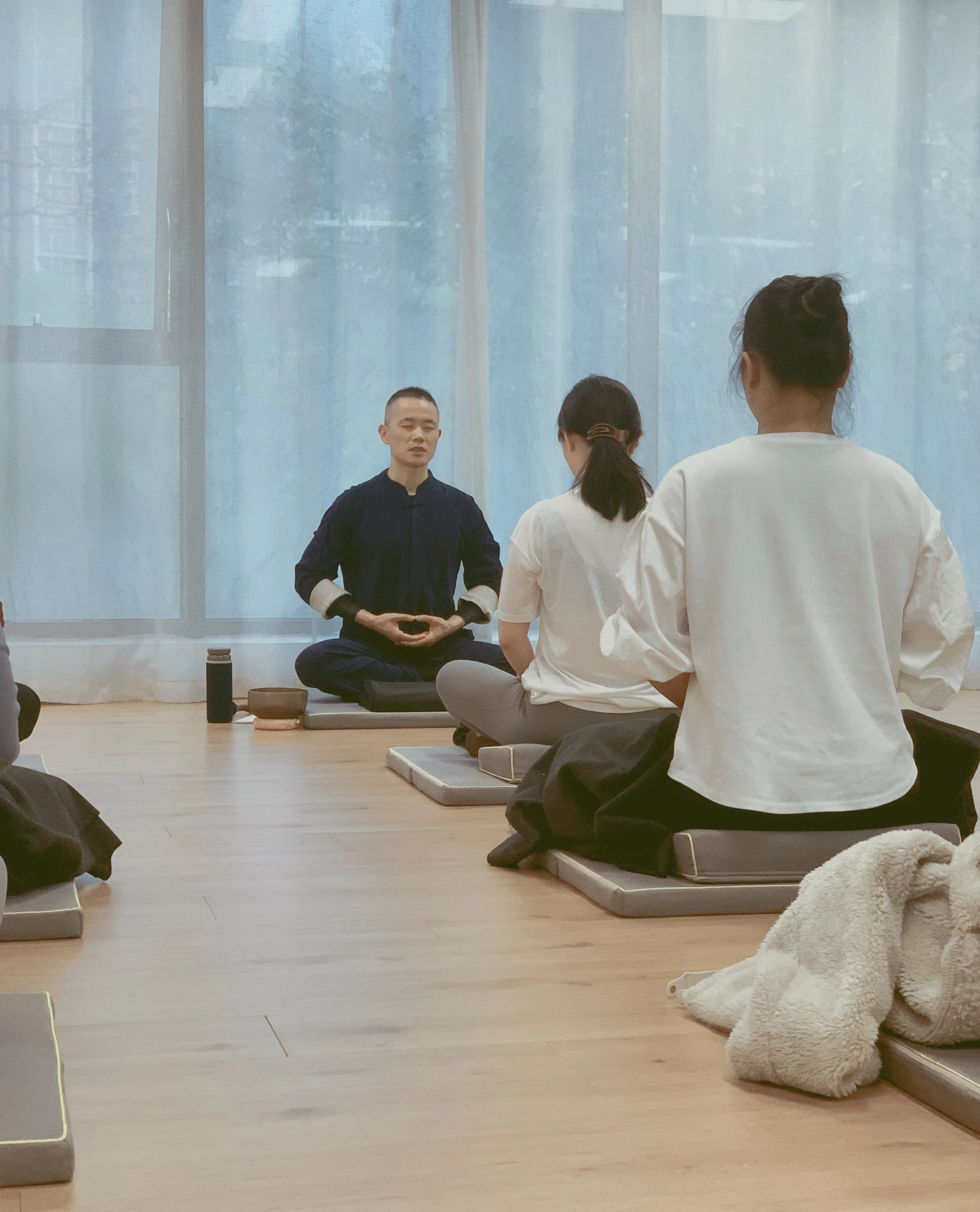A male Pilates instructor at a Pilates studio is teaching students how to meditate.